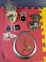 Photo of assorted jewelry laid out on a red/yellow foam puzzle mat including necklaces, rings, earrings, and decorative boxes.