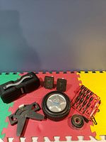 Lot of items including Bluetooth speaker, car pedals, hubcap, and a red tool bit set with tape measure on a colorful foam mat