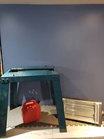 Green metal saw stand, small red gas can, and electric heater visible on floor against wall.