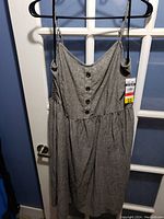 Front view of gray dress hanging on black hanger on white door, showing button-front and gathered skirt