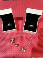 Full view of two rings in white Pandora boxes and a charm bracelet laid on a red textured surface