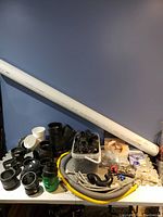 Displays various black plastic pipe fittings, a long white PVC pipe, flexible hoses, metal connectors, and small plumbing parts spread on a table.