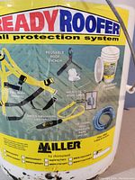 Photo showing the Ready Roofer fall protection system bucket decal with components listed and illustrated including harness, anchor, lanyard, rope grab, rope and container details.