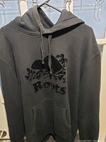 Front view of black Roots hoodie with beaver and branch logo on chest and front pocket