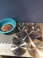 Set of six 10-inch Ryobi circular saw blades with various tooth counts and a blue bowl containing assorted grinding/cutting discs.