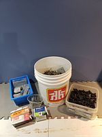 Photo of white bucket with screws plus containers with black fasteners and blue bin with staples