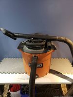 Front and side view of a Ridgid orange and black shop vac with hose and power cord.