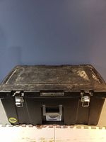 Black plastic tool storage bin with metal latches and handle visible from the front.