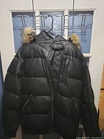 Front view of the black puffer jacket with faux fur hood, showing the quilted design, zippered pockets, and button closure.
