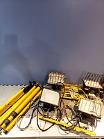 Four yellow work lights on tripods arranged against wall, cords visible. Close view shows condition and items in lot.