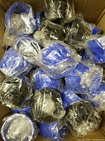 Box containing more than 50 polyethylene pipe connectors in blue and black colors, individually wrapped in plastic bags.