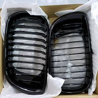 A pair of glossy black BMW kidney grills placed inside protective white cloth within a cardboard box, showing the front grille design with horizontal slats.