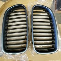 Pair of BMW F10 kidney front grilles with horizontal black slats and Neptune Blue painted surround placed on plastic.