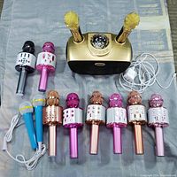 Photo of nine-piece karaoke set including gold karaoke machine with disco ball, two gold mounted microphones, and seven handheld microphones in various metallic colors with some cords