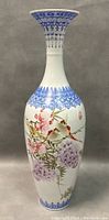 Full view of the tall hand painted vase showing floral and bird designs with blue decorative borders.