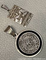Two Mexican 925 silver pendants shown together, rectangular Mayan figure and round Aztec calendar.