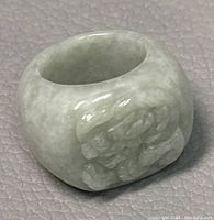 Close-up image of solid green jade ring showing carved design on the band and polished, glossy surface.