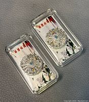 Two Chinese 999 silver filigree miniature bars housed in clear acrylic display cases showing front design with colorful accents and Chinese characters on decorative background.