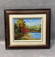 Framed oil painting depicting a lake and colorful trees in fall with a wooden frame and linen mat.