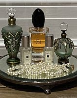 Full lot on mirror topped silver stand, showing all perfume bottles, faux pearl necklace spread in front.