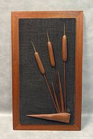 Front view of the mid-century modern teak wood framed wall art with carved cattails on black textured background.
