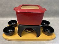 Front view of the entire Swissmar fondue set showing red enamel pot on black stand, wooden tray and four black bowls