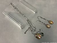 Double-strand silver-tone necklace and matching drop earrings displayed on clear stands, showing details of pendants and charms without direct light.