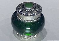 Close-up of emerald green glass snuff bottle with detailed silver lid topped by green stone, showing overall condition