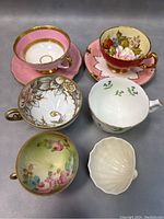 Six items arranged: two teacup and saucer sets, three orphan teacups, one shell-shaped sugar bowl