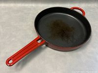 Angled side view of the red enameled cast iron frying pan showing the black interior cooking surface with wear marks.