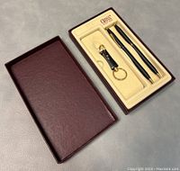 Box open showing black mechanical pencil, ballpoint pen, and personalized keychain with gold-tone details inside fitted cream insert marked CROSS