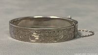 Front view of vintage sterling silver hinged bangle bracelet showing detailed etching and safety chain.