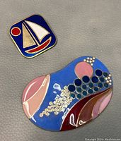 Photo showing the full kidney-shaped pendant and square sailboat brooch on a plain background