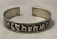 Front angle showing raised Tibetan mantra and turquoise stones on the cuff bracelet, with one stone missing.