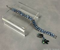 Blue crystal Weiss bracelet alongside Sherman clip-on earrings on an acrylic display stand, showing details of stones and setting.