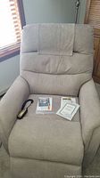 Front view of taupe Berkline lift chair with remote control and manuals placed on seat, showing upholstery and condition.