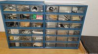 Two blue plastic storage units with multiple transparent drawers containing small hardware parts and accessories