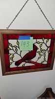 Front view of cardinal stained glass panel hanging on the wall with blue tape noting lot number and dimensions.