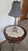 Dark wood circular claw foot side table with crocheted doily and black metal base lamp with black fabric shade, photo angle from front side