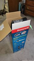 Front and side view of the Honeywell air purifier inside its original box placed on carpet.