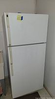 Full view of white Hotpoint refrigerator showing top freezer and bottom fridge doors with beige handles.