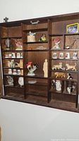 Wall-mounted wooden display case for miniatures containing animal figurines, thimbles, and other small collectibles.