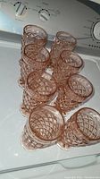 Eight pink pressed glass drinking glasses displayed together showing diamond pattern and scalloped base.
