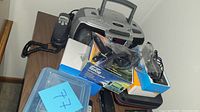 Photo showing portable stereo, navigation system boxes, corded phone, and accessories on a small table.