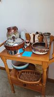 View of various signed pottery and ceramic items arranged on a small wooden table including pitchers, baskets, bowls, and decorative pieces.