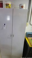 Front view of white slim metal storage cabinet with two doors and label on doors