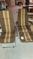 Pair of vintage metal outdoor folding chairs with padded brown cushions and vertical multi-color stripes, showing the full form and details of cushioning and metal frames.