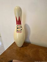Brunswick bowling pin standing on wood surface against wall, cream white with red crown logo and Brunswick branding