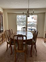 Full view of vintage Bassett Versailles wood dining table with six chairs, placed in dining room with window and chandelier overhead.