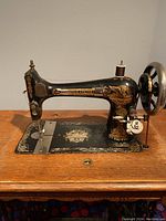 Close-up of Singer treadle sewing machine on wooden table showing gold detailing on machine.